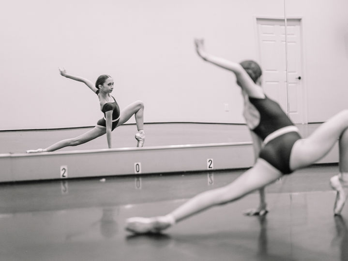 Ballet student practicing a lunge in front of the studio mirror